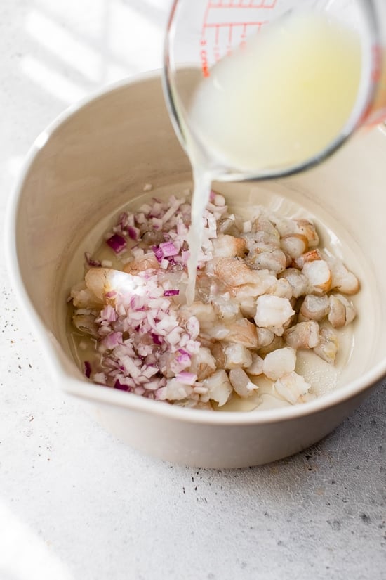 Shrimp in a bowl with lime juice, salt and red onion.