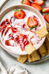 Overhead view of a bowl of strawberry cheesecake dip surrounded by mini graham crackers.