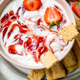 Overhead view of a bowl of strawberry cheesecake dip surrounded by mini graham crackers.