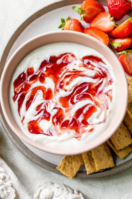 Creamy strawberry cheesecake dip tastes just like cheesecake in dip form! Serve with fresh fruit or graham crackers as a snack or appetizer. Overhead view of a bowl of strawberry cheesecake dip surrounded by mini graham crackers and fresh strawberries.