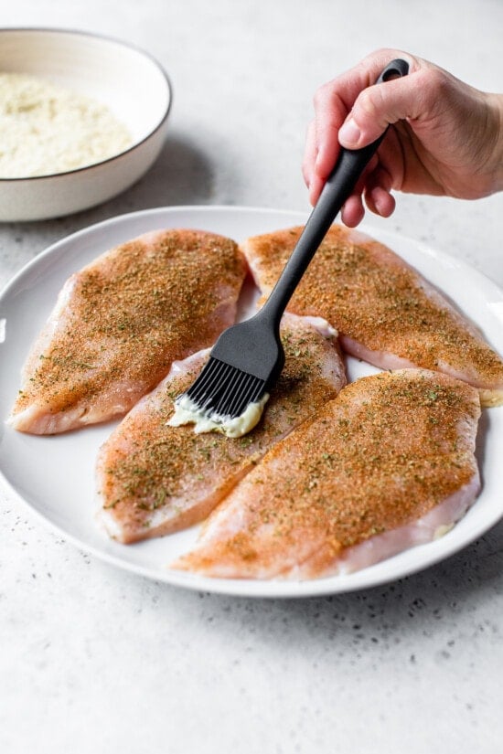 seasoned chicken breast with mayo being spreaded on top