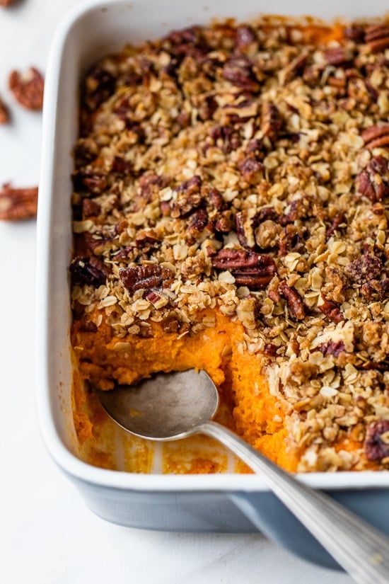 This lightened up Sweet Potato Casserole is made with roasted sweet potatoes and a praline topping for a crowd-pleasing Thanksgiving side! Spoon digging into sweet potato casserole with praline topping in baking dish.