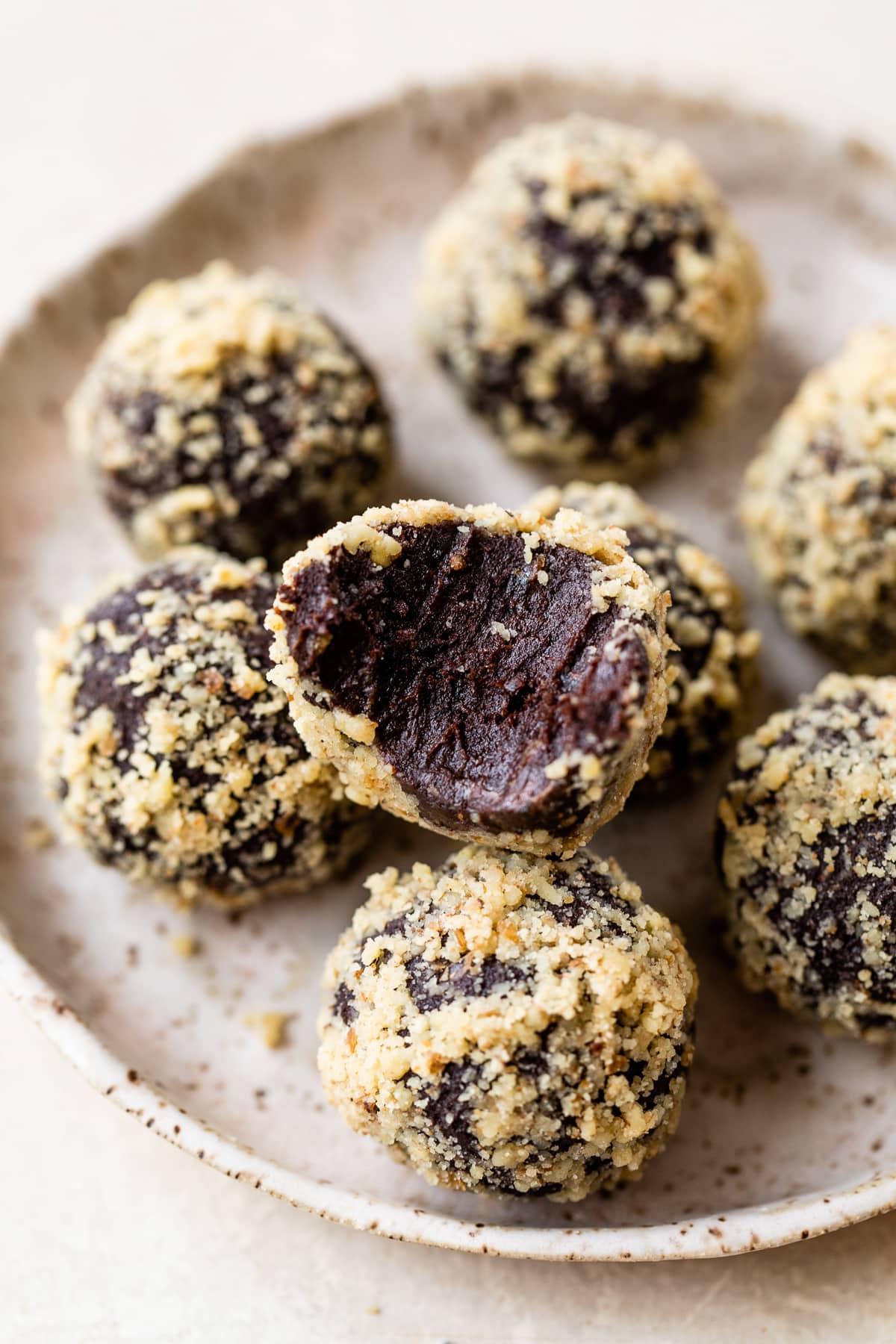 A plate of chocolate date balls, one with a bite missing to show the fudgy inside.
