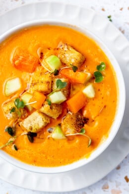 Overhead view of a bowl of gazpacho topped with fresh chopped cucumber, tomato, and crunchy croutons.