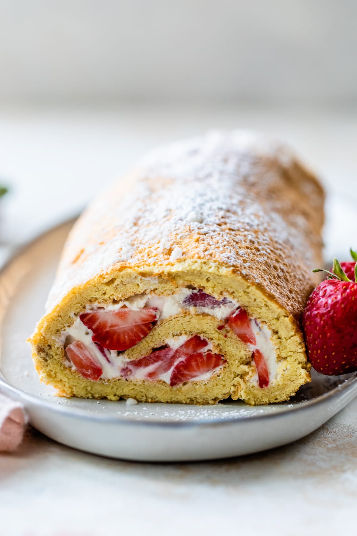 This Strawberry Swiss Roll features a soft sponge cake, sweet cream, and fresh strawberries. So simple & perfect when berries are in season. Strawberry Swiss Roll on a plate