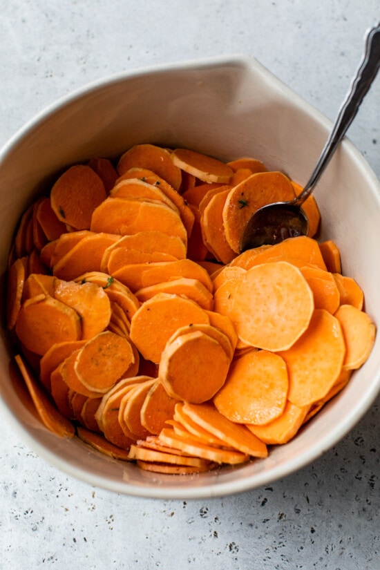 Make sweet potatoes au gratin inspired by Pommes Anna, a French dish of creamy, thinly sliced potatoes topped with melted Gruyere cheese. Thinly sliced sweet potatoes in a bowl.