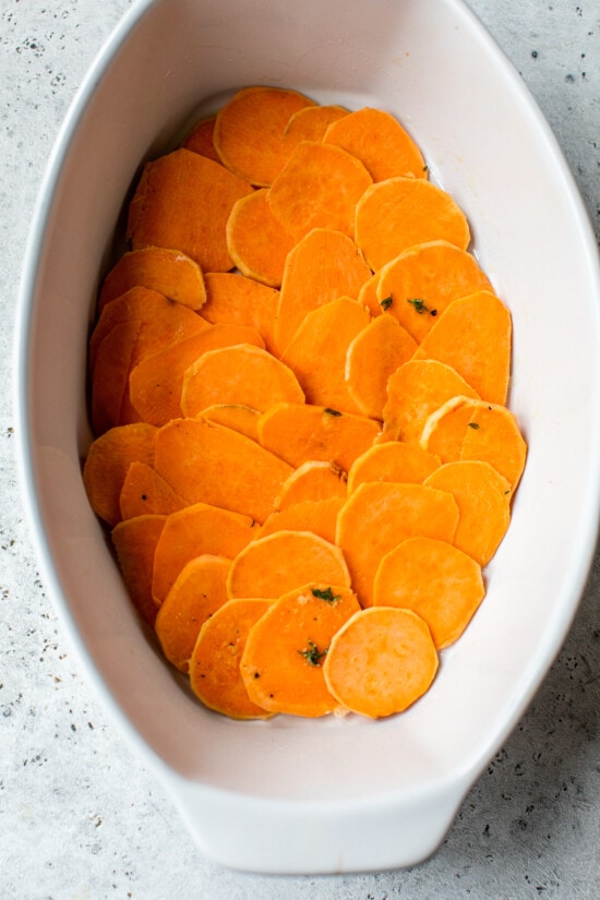 Make sweet potatoes au gratin inspired by Pommes Anna, a French dish of creamy, thinly sliced potatoes topped with melted Gruyere cheese. Thin sweet potato slices layered in an oval casserole dish.