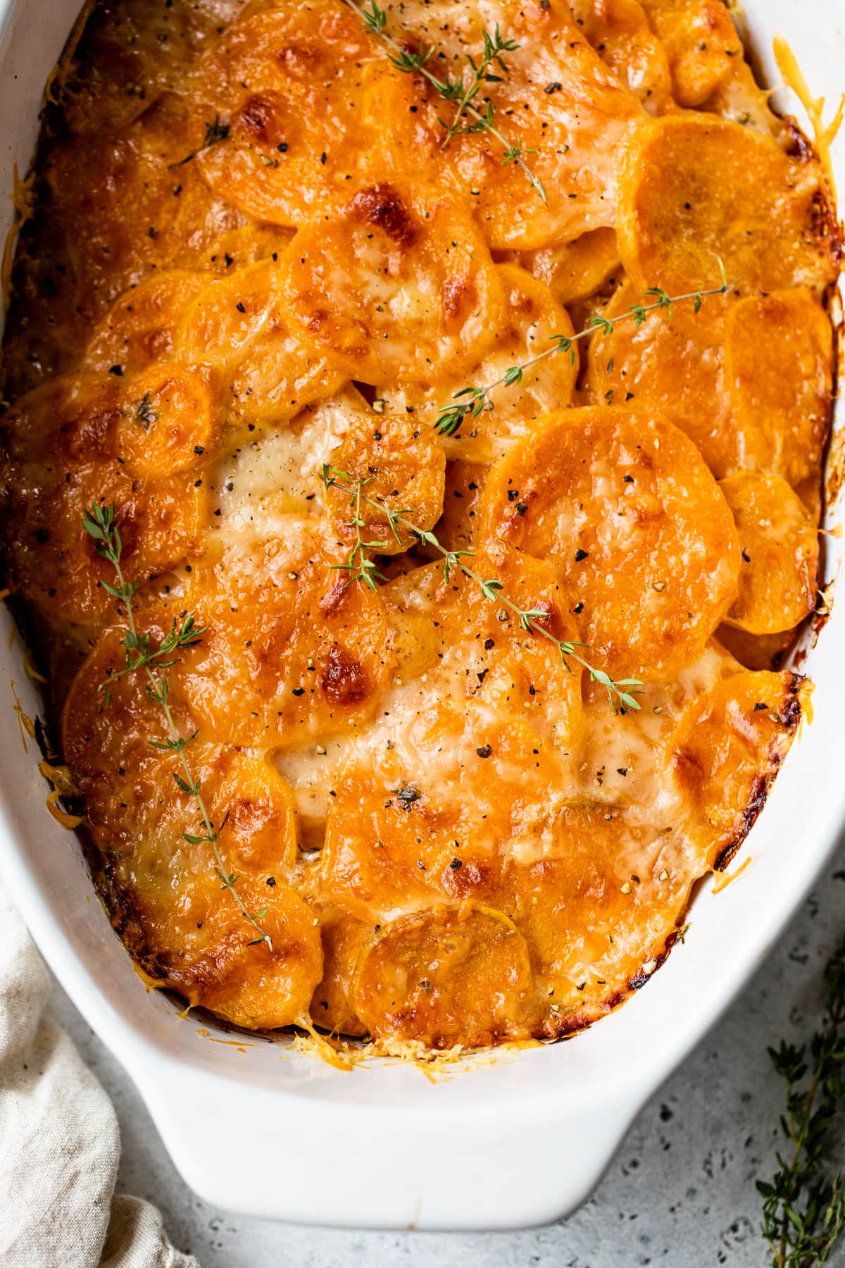 Make sweet potatoes au gratin inspired by Pommes Anna, a French dish of creamy, thinly sliced potatoes topped with melted Gruyere cheese. Overhead view of sweet potato gratin in an oval casserole dish.