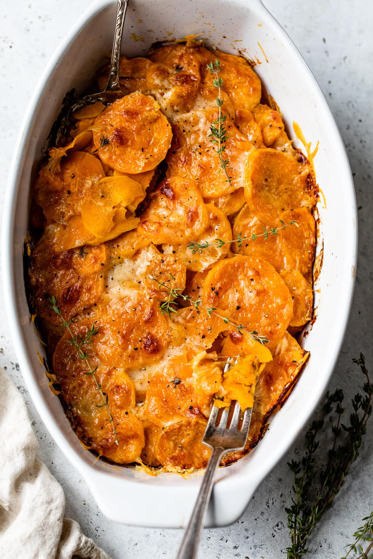 Make sweet potatoes au gratin inspired by Pommes Anna, a French dish of creamy, thinly sliced potatoes topped with melted Gruyere cheese. Overhead view of a fork resting in a casserole dish of sweet potatoes au gratin.