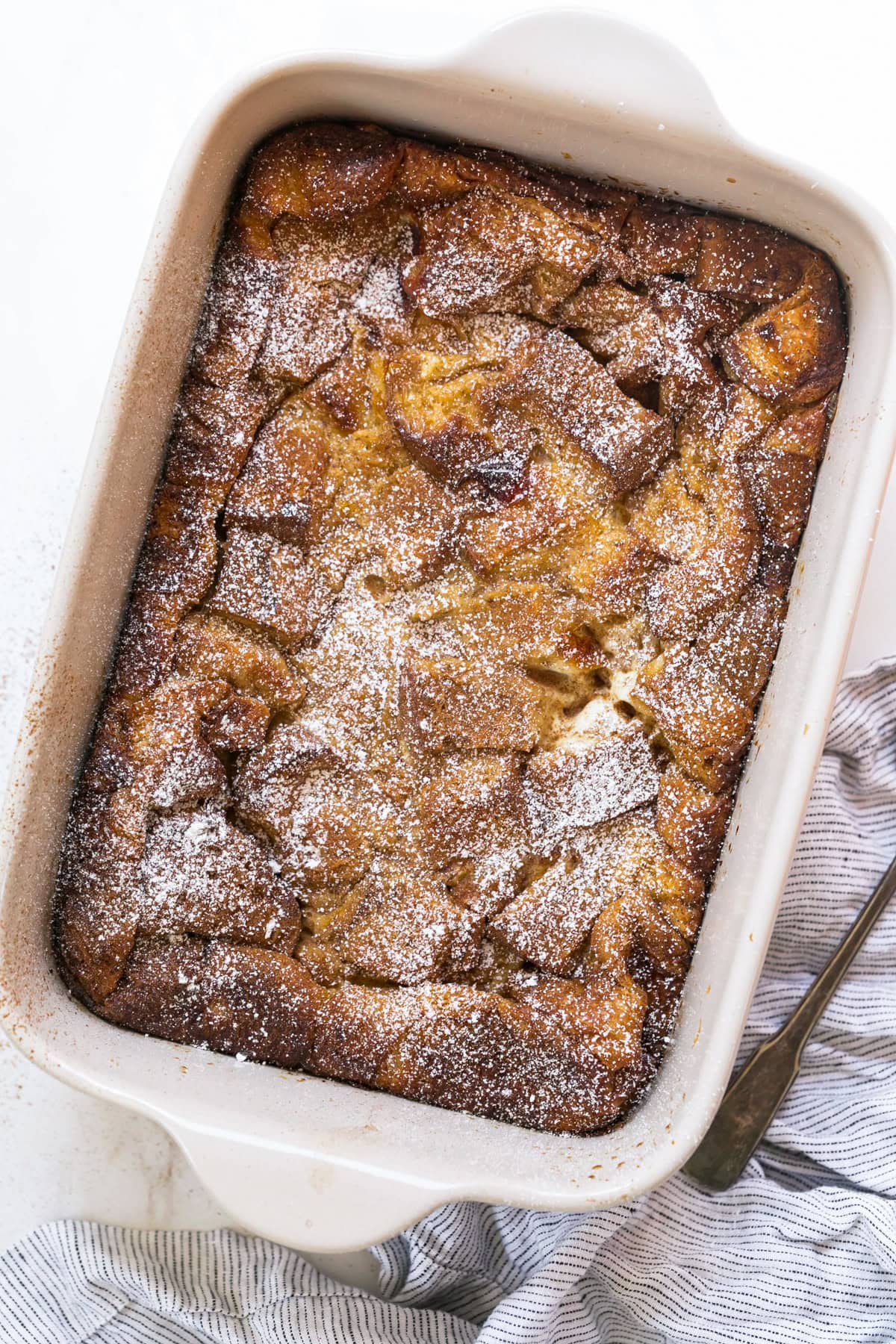This overnight crème brûlée French toast bake is an easy make-ahead breakfast with fluffy challah, eggy custard, and only 15 minutes of prep! Overhead view of a baked creme brulee French toast casserole dusted with powdered sugar.