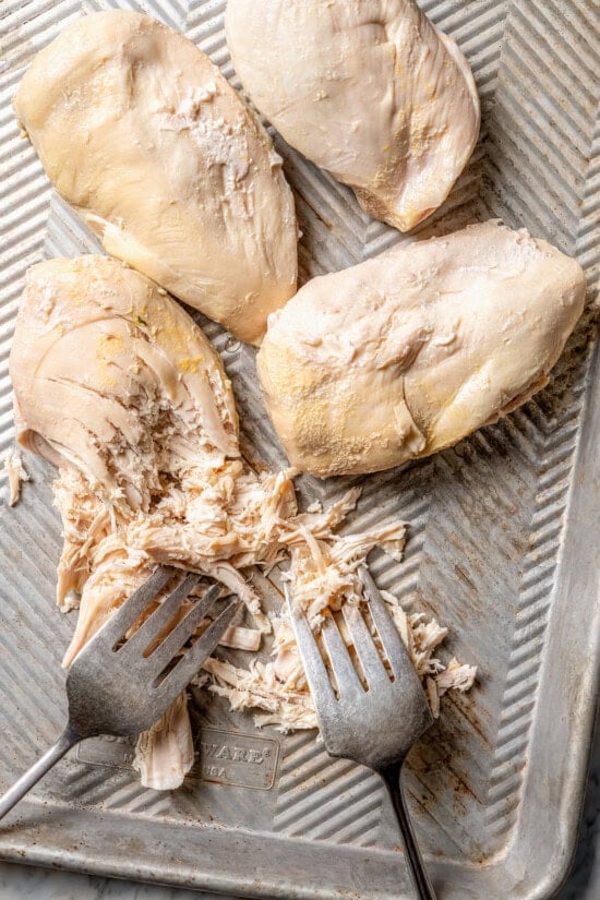 This slow cooker shredded chicken recipe is juicy, tender, and flavorful. It's a hands-off cooking method perfect for meal prep! Forks shredding cooked chicken breasts