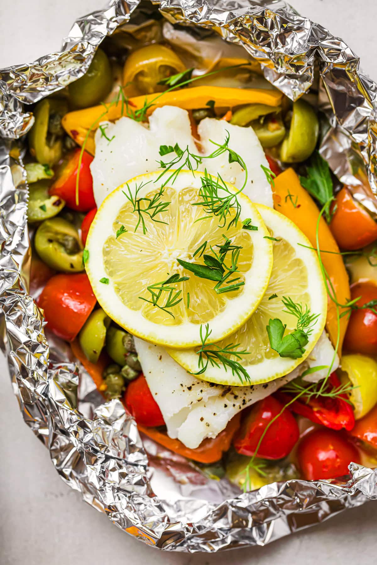 Vegetables, fish, lemon slices, and fresh herbs in foil packet.