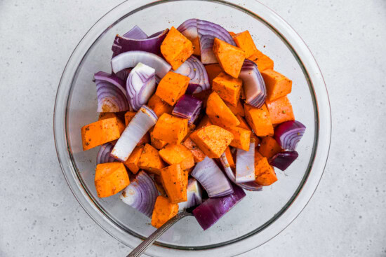 Potatoes, red onion in a bowl with seasoning.