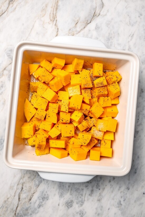 Baked butternut squash is layered with creamy goat cheese, shallots, and pistachios in this cozy side dish recipe. Perfect for the holidays! Seasoned butternut squash in baking dish.