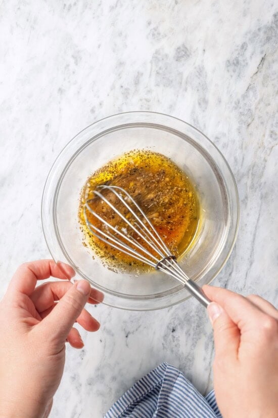 This homemade Greek salad dressing recipe blends simple pantry ingredients into a bright, zippy dressing you’ll want to pour on everything! Whisking Greek salad dressing in small glass bowl.