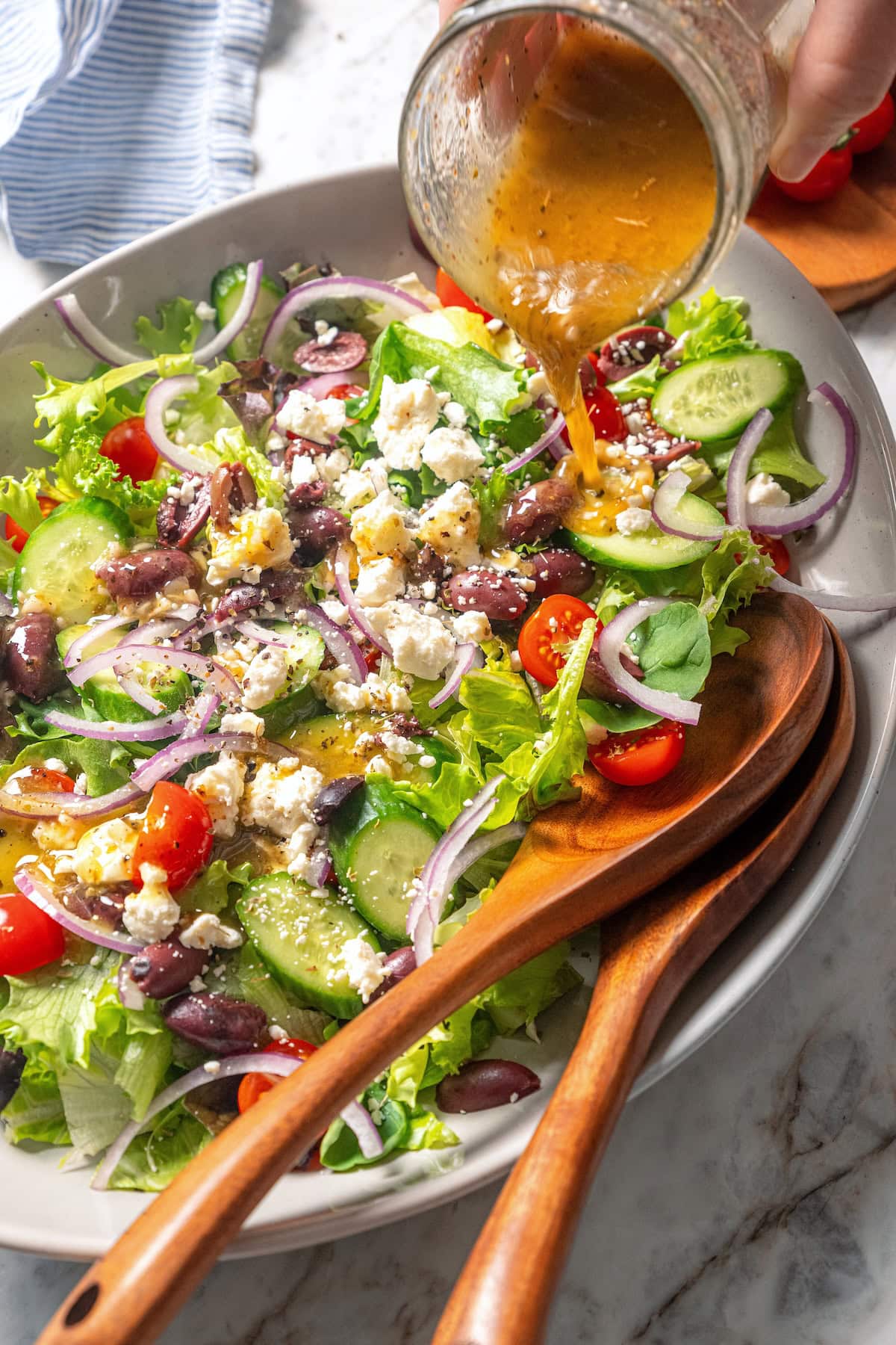 This homemade Greek salad dressing recipe blends simple pantry ingredients into a bright, zippy dressing you’ll want to pour on everything! Pouring Greek salad dressing over bowl of salad.